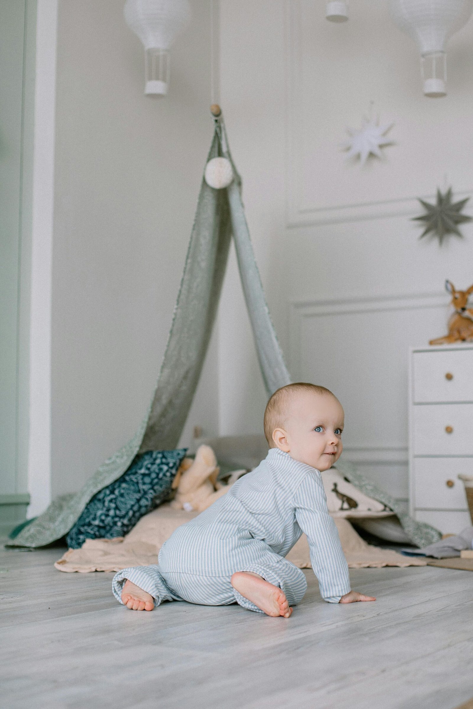 Baby in striped outfit crawling in a stylish nursery with a cozy tent and soft decor.